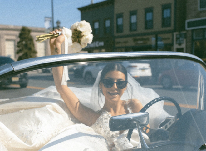 bride riding car and holding out white rose bouquet